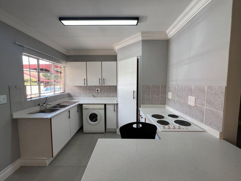 A clean, functional kitchen featuring white cabinetry, laminate countertops, a built-in electric hob, tiled backsplash, and an integrated washing machine.