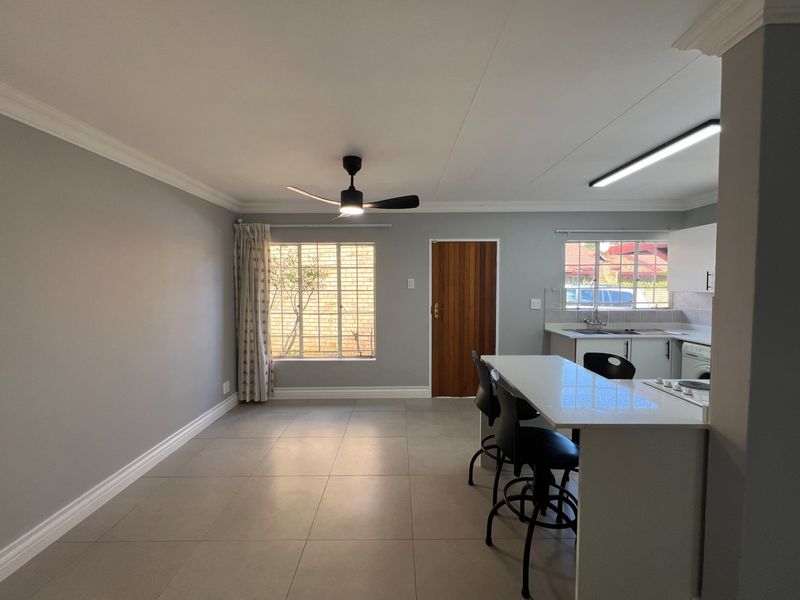 Open-plan living and kitchen area featuring neutral tiled flooring, modern ceiling fan, and a functional kitchen island with integrated cabinetry.