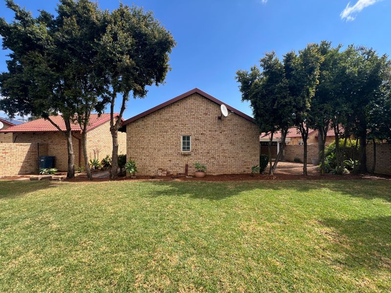 A view of the rear exterior of the townhouse, featuring a brick facade, tiled roof, and a well-maintained lawn area.