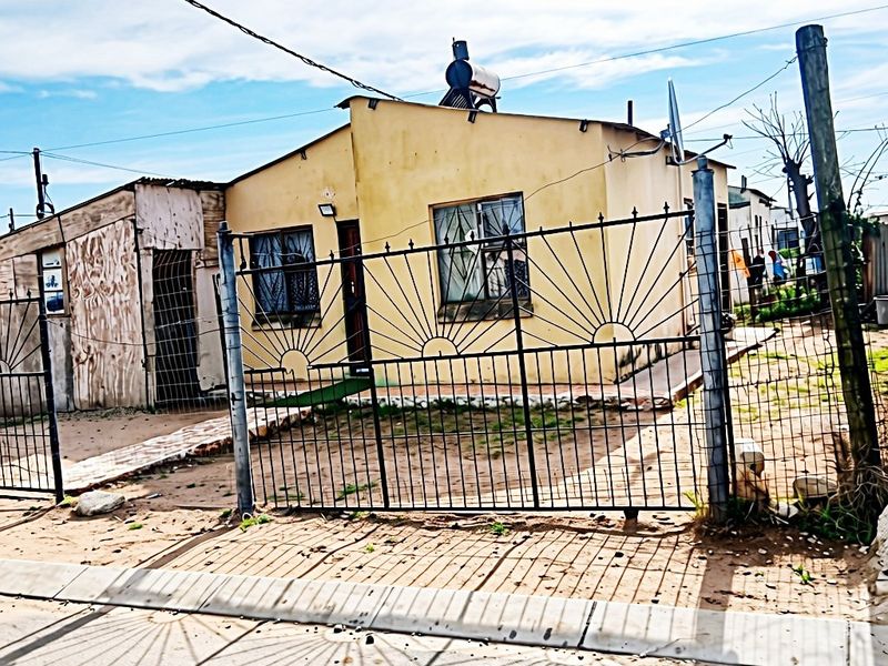 Front view of a single-story house featuring a solar water heater, metal security gate, and perimeter wire fencing.