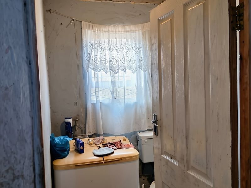 A small laundry area featuring a tiled ceiling and basic plumbing connections, currently in need of significant renovation and cosmetic repair.