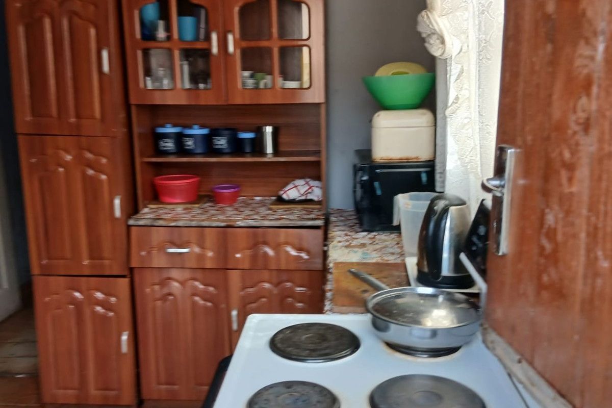 A compact kitchen featuring dated wooden cabinetry, laminate countertops, and a freestanding electric stove with tiled flooring.