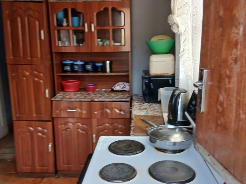 A compact kitchen featuring dated wooden cabinetry, laminate countertops, and a freestanding electric stove with tiled flooring.