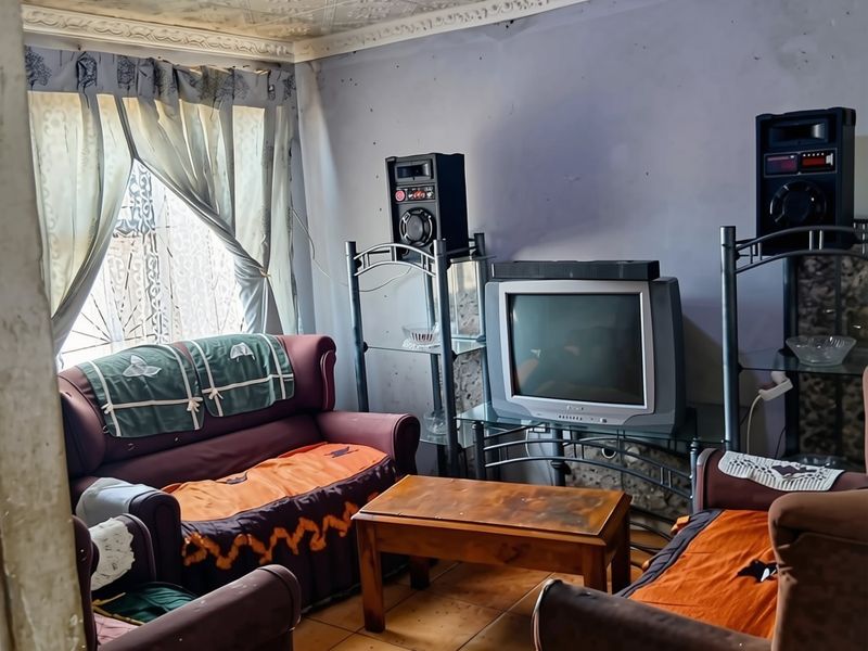 A living room featuring decorative ceiling tiles, ceramic floor tiling, and wall surfaces in need of maintenance and repainting.