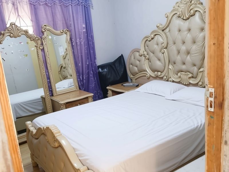 A bedroom featuring laminate flooring and a curtain rod, currently furnished with a large bed and vanity mirror.