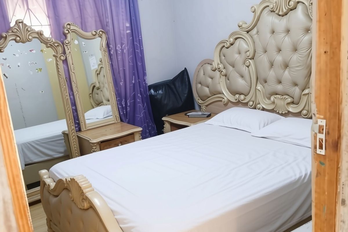 A bedroom featuring laminate flooring and a curtain rod, currently furnished with a large bed and vanity mirror.