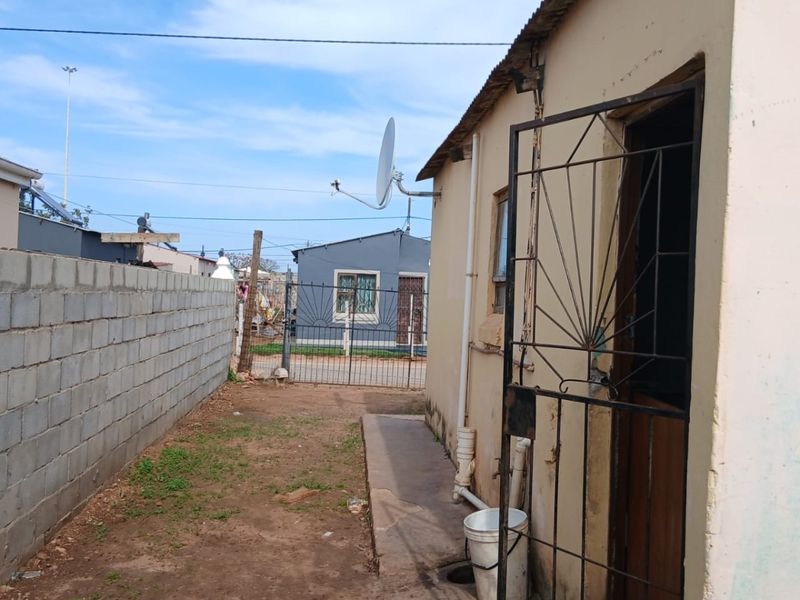 Rear exterior view of the property featuring a concrete block boundary wall, metal security gate, and basic external infrastructure.