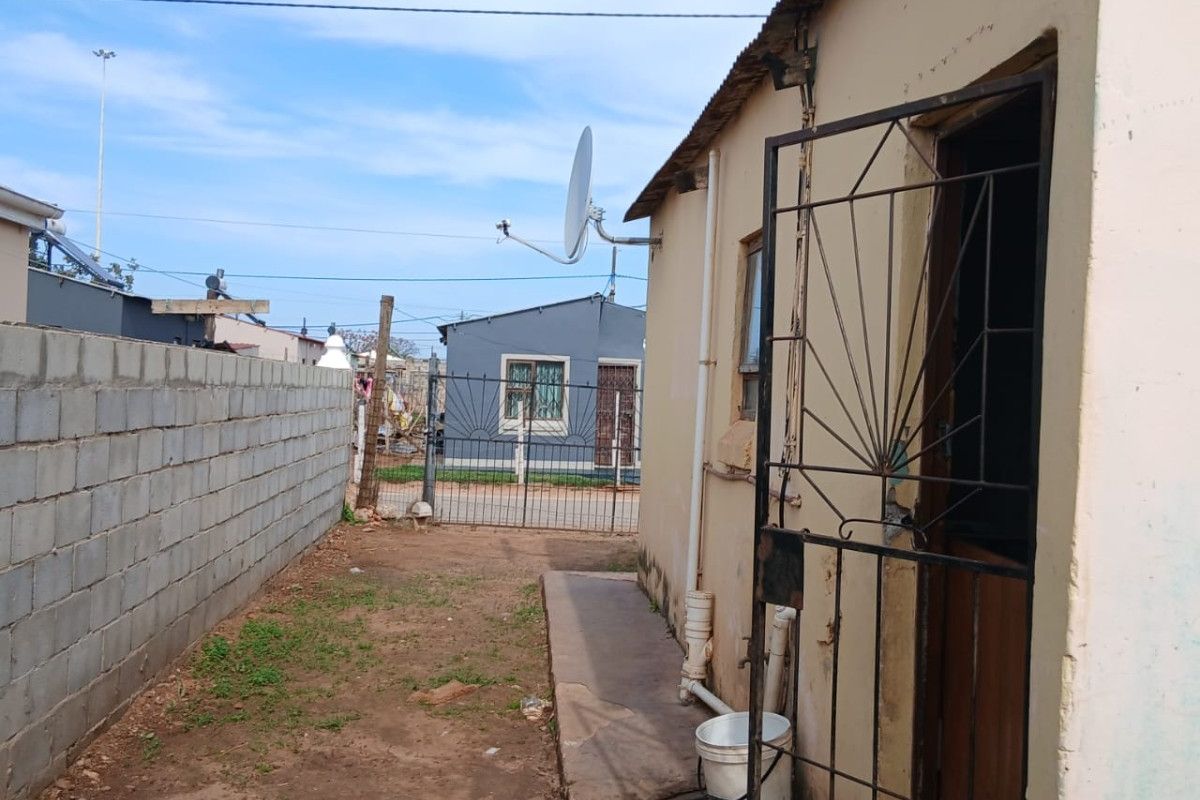 Rear exterior view of the property featuring a concrete block boundary wall, metal security gate, and basic external infrastructure.