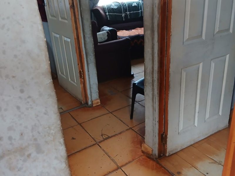 A narrow hallway featuring tiled flooring and panel doors, showing signs of significant wear and requiring maintenance or renovation.