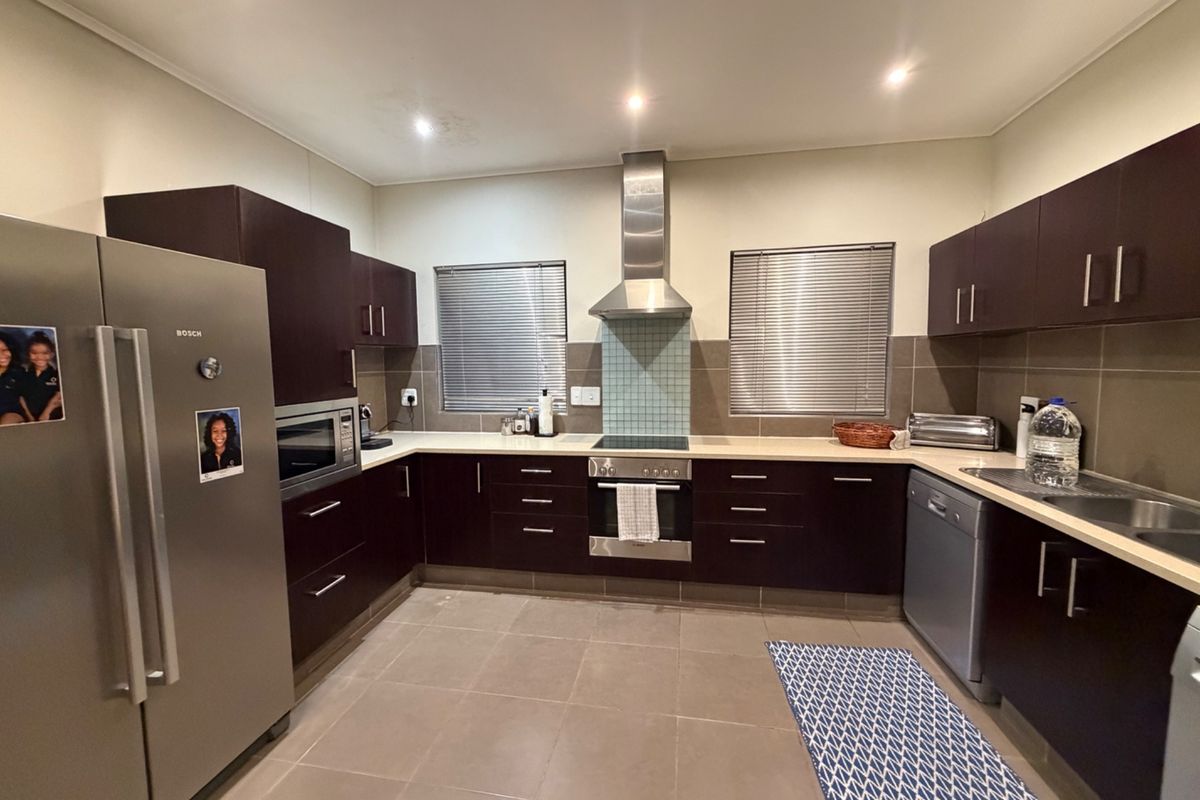 A functional kitchen featuring dark wood cabinetry, stone countertops, stainless steel appliances, and a tiled backsplash with ample storage space.