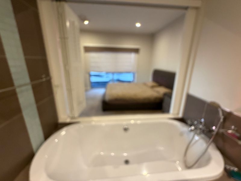A bathroom featuring a built-in bathtub with a shower mixer, looking through an opening into an adjacent bedroom area.