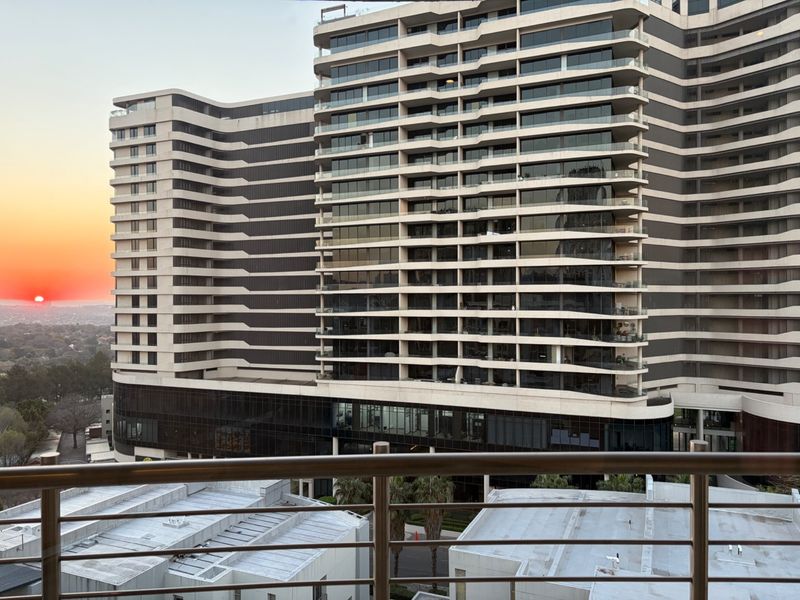 A scenic sunset view overlooking the modern architectural facade of a large apartment complex from a private balcony.