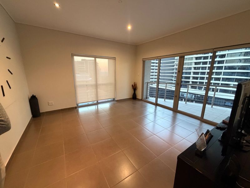 Spacious, light-filled living area featuring neutral tiled flooring, recessed lighting, and large sliding glass doors leading to a private balcony.