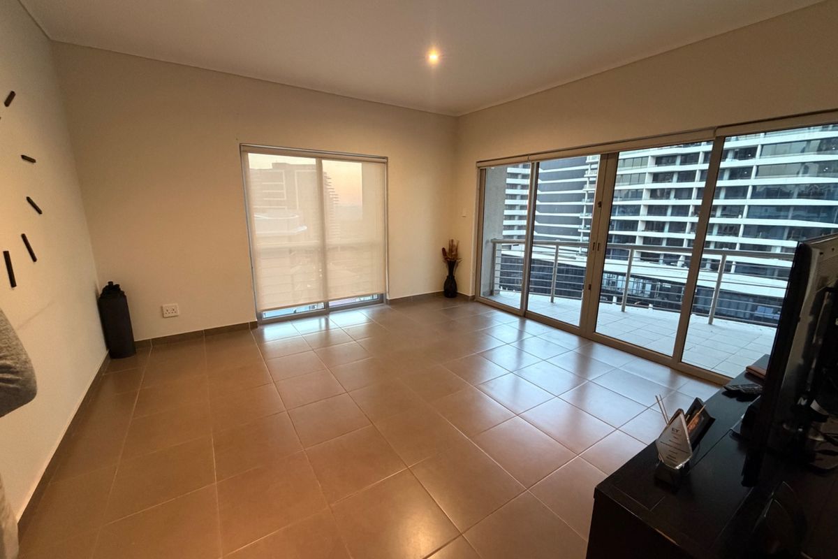 Spacious, light-filled living area featuring neutral tiled flooring, recessed lighting, and large sliding glass doors leading to a private balcony.