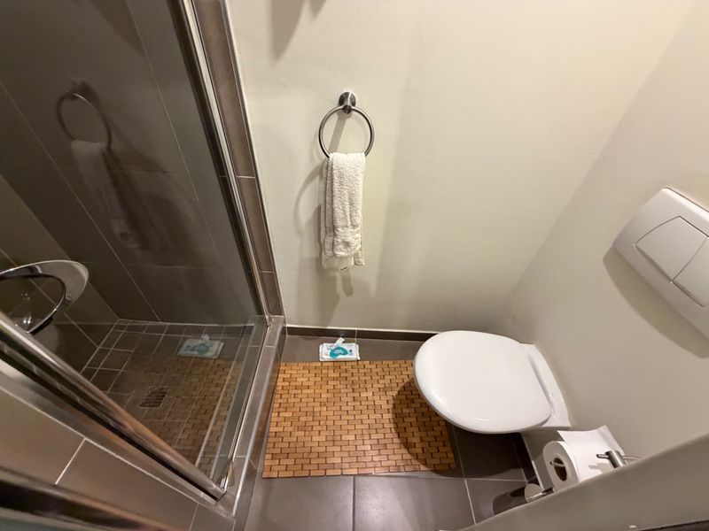 A compact bathroom featuring a glass-enclosed shower, wall-mounted toilet, and neutral tiled flooring.