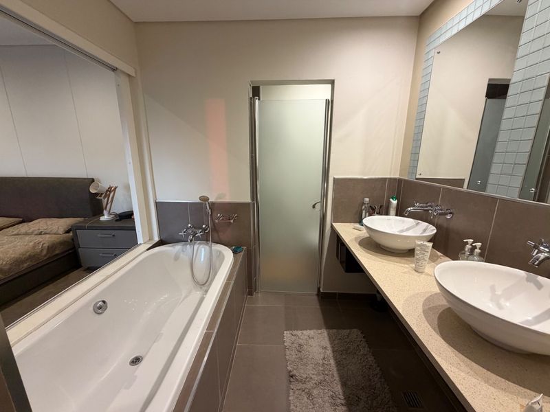 Modern bathroom featuring a double vanity with vessel sinks, a built-in bathtub, and a separate shower enclosure with a frosted glass door.