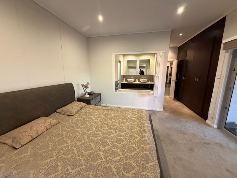 Spacious bedroom featuring built-in cupboards, recessed lighting, and a unique open-view window connecting to the en-suite bathroom.