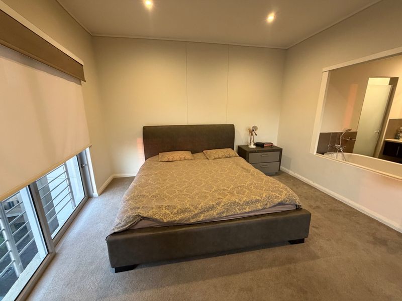 A spacious bedroom featuring neutral walls, carpeted flooring, recessed lighting, and an internal window looking into the adjoining bathroom area.