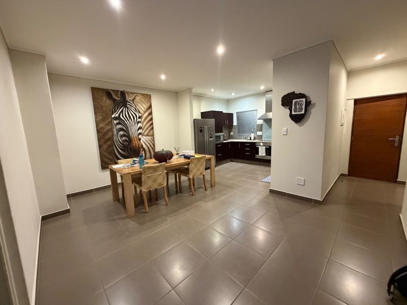 Open-plan living and kitchen area featuring tiled flooring, modern dark cabinetry, built-in appliances, and recessed lighting throughout the space.