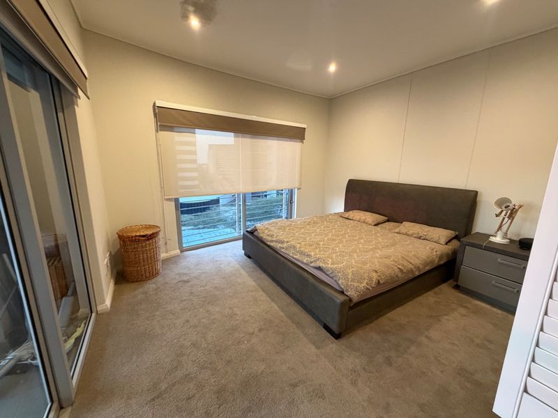 A carpeted bedroom featuring recessed downlights, roller blinds, and a sliding glass door leading to an outdoor area.