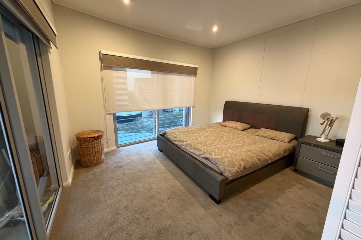 A carpeted bedroom featuring recessed downlights, roller blinds, and a sliding glass door leading to an outdoor area.