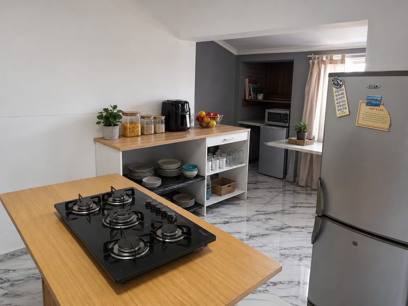 A functional kitchen area featuring a central island with a built-in gas hob, marble-look tiled flooring, and open shelving for storage.