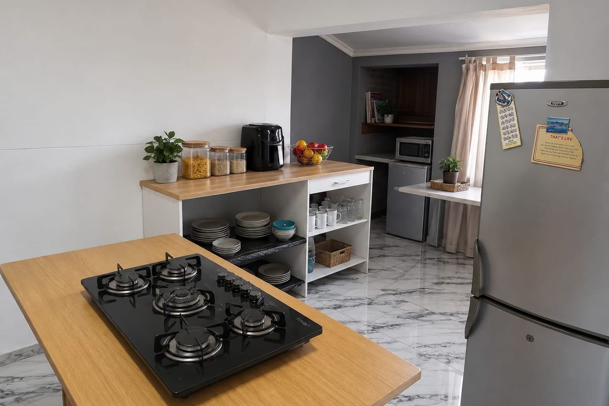 A functional kitchen area featuring a central island with a built-in gas hob, marble-look tiled flooring, and open shelving for storage.