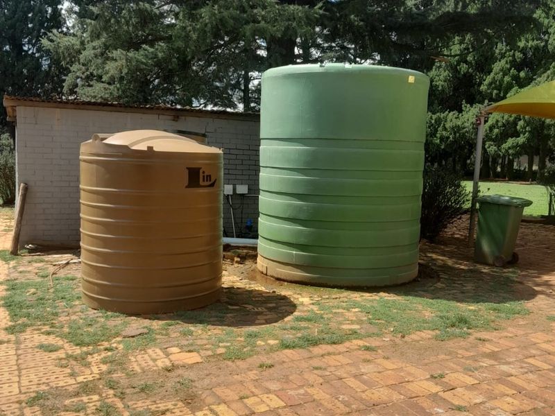 Outdoor area featuring two large water storage tanks situated on a brick paved surface adjacent to a brick outbuilding.