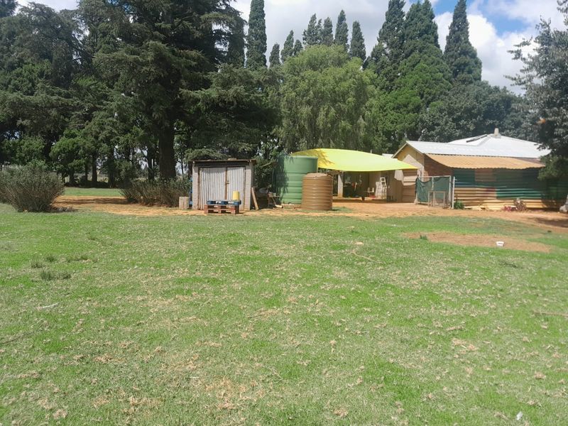 A view of the farm property rear yard featuring water storage tanks, a corrugated metal shed, and a simple farm building structure.