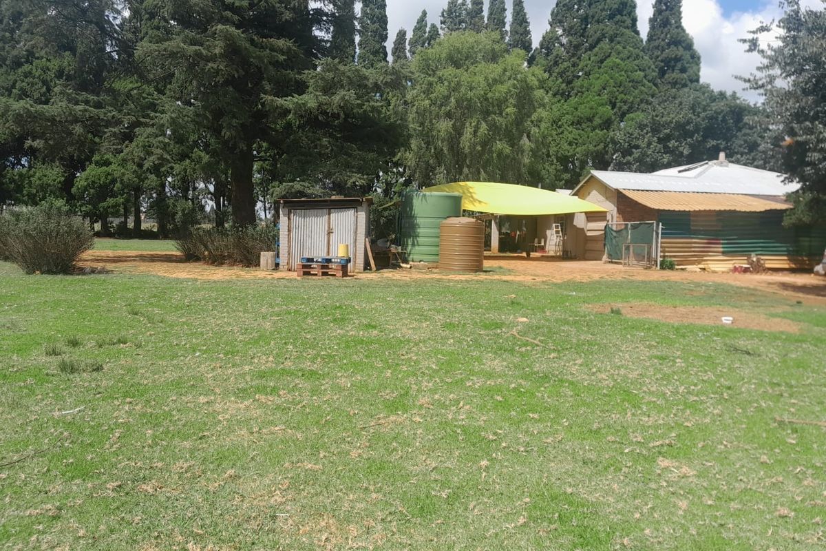 A view of the farm property rear yard featuring water storage tanks, a corrugated metal shed, and a simple farm building structure.