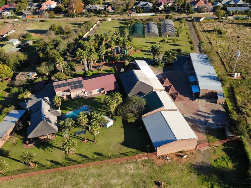 Aerial view of a commercial property featuring multiple buildings, a swimming pool, solar panels, greenhouses, and extensive landscaped grounds.