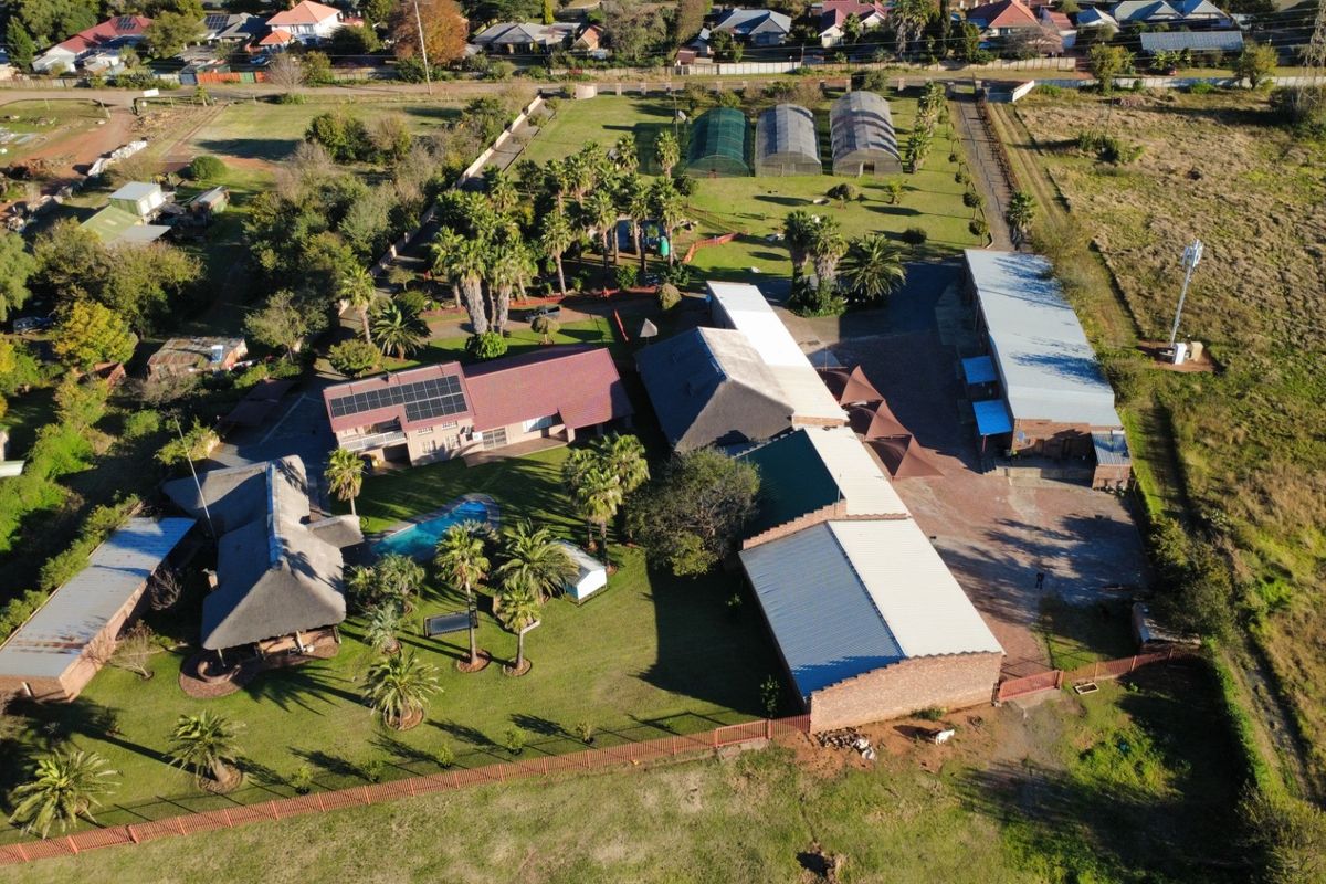 Aerial view of a commercial property featuring multiple buildings, a swimming pool, solar panels, greenhouses, and extensive landscaped grounds.