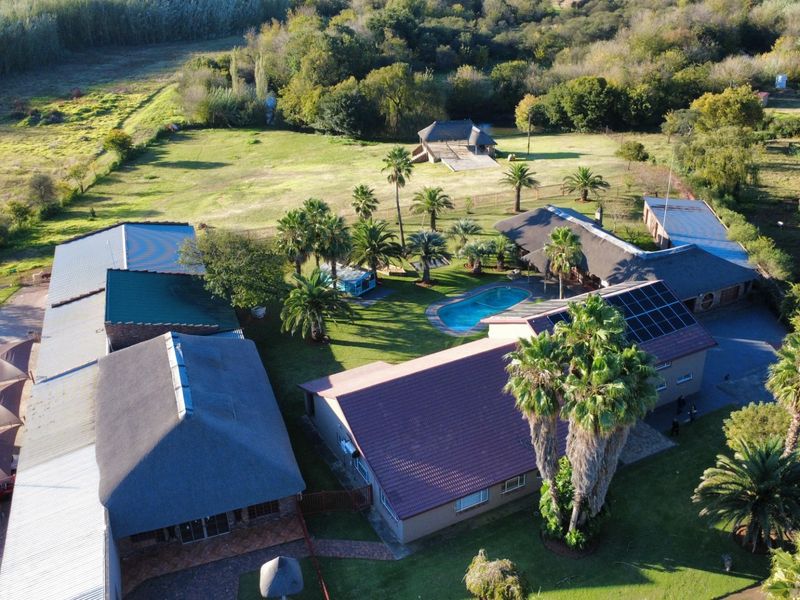 Aerial view of a commercial property featuring multiple buildings, a swimming pool, solar panels, and extensive landscaped grounds.