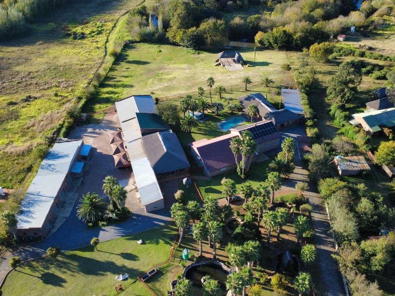 Aerial view of a commercial property complex featuring multiple buildings, a swimming pool, solar panel installations, and extensive landscaped grounds.