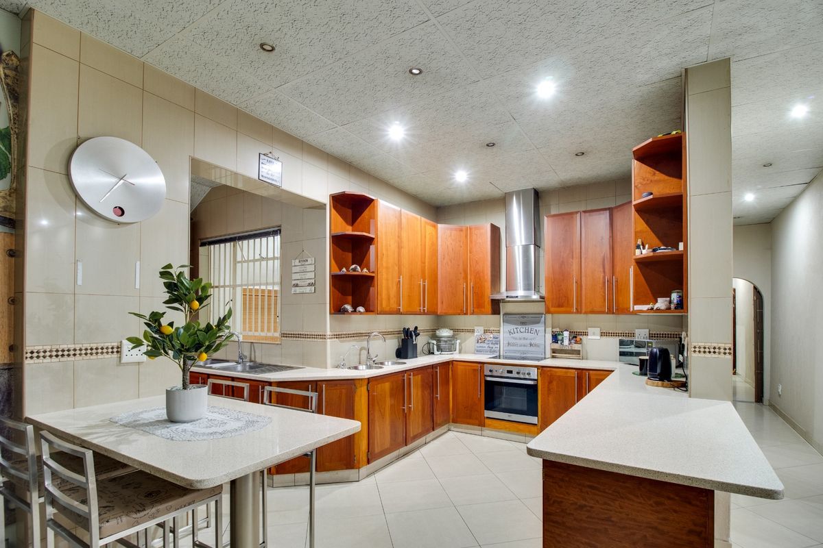 A functional kitchen featuring warm wooden cabinetry, stone countertops, a built-in oven with extractor fan, and a double stainless steel sink.