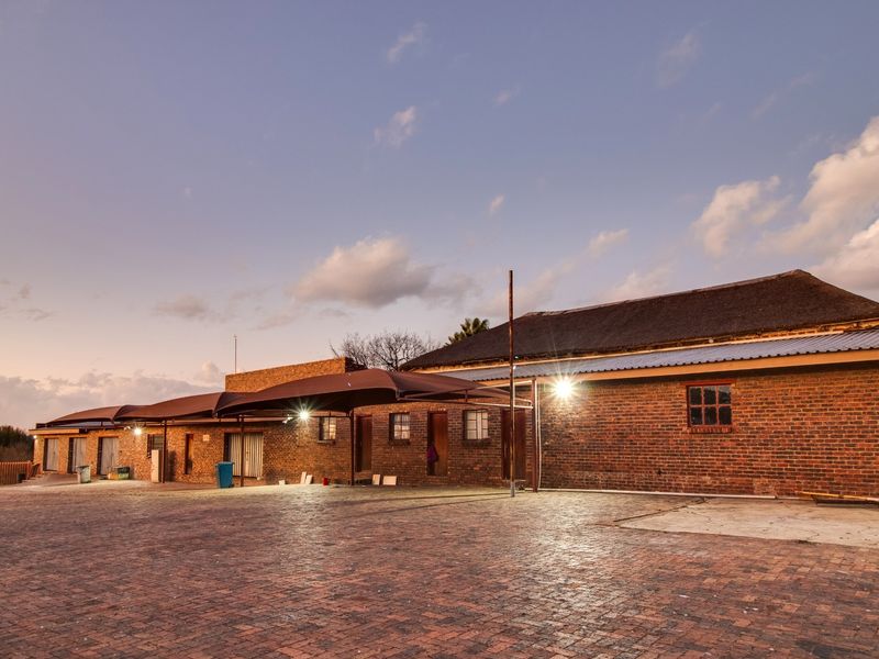 A wide-angle view of a commercial property featuring a brick facade, thatched roof, and a large paved parking area with shade cloth carports.
