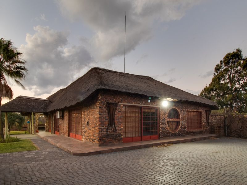 A commercial property featuring a traditional thatch roof, face brick exterior, and a paved driveway with secure gated access.