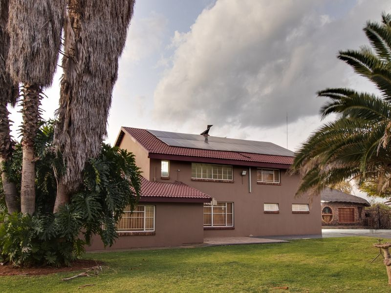 Rear view of a commercial property featuring a tiled roof with installed solar panels, brick exterior walls, and security-fitted windows set in a garden.