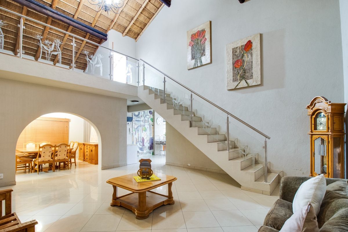 Spacious living area featuring a prominent staircase with glass balustrades, high thatched ceilings, and an arched entrance leading to the dining space.