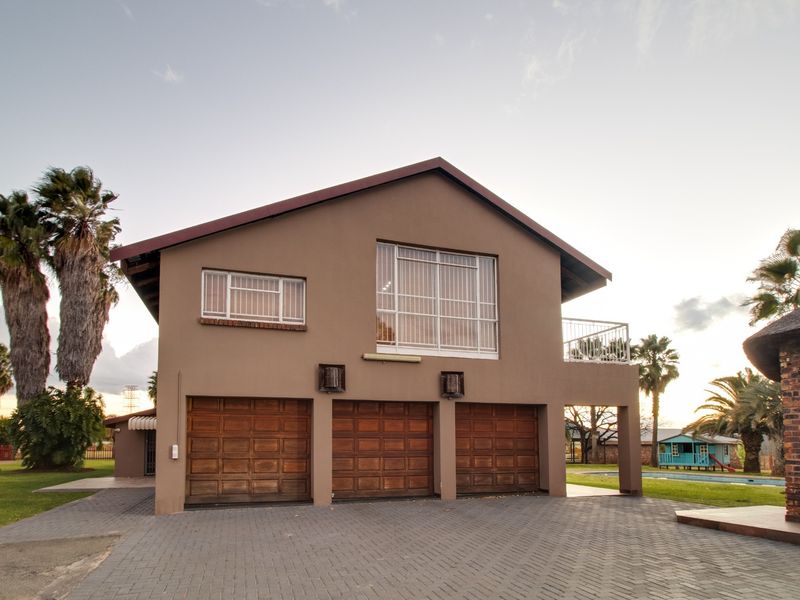 Front elevation of a commercial property featuring a triple garage, paved driveway, and an upper-level balcony with exterior lighting.