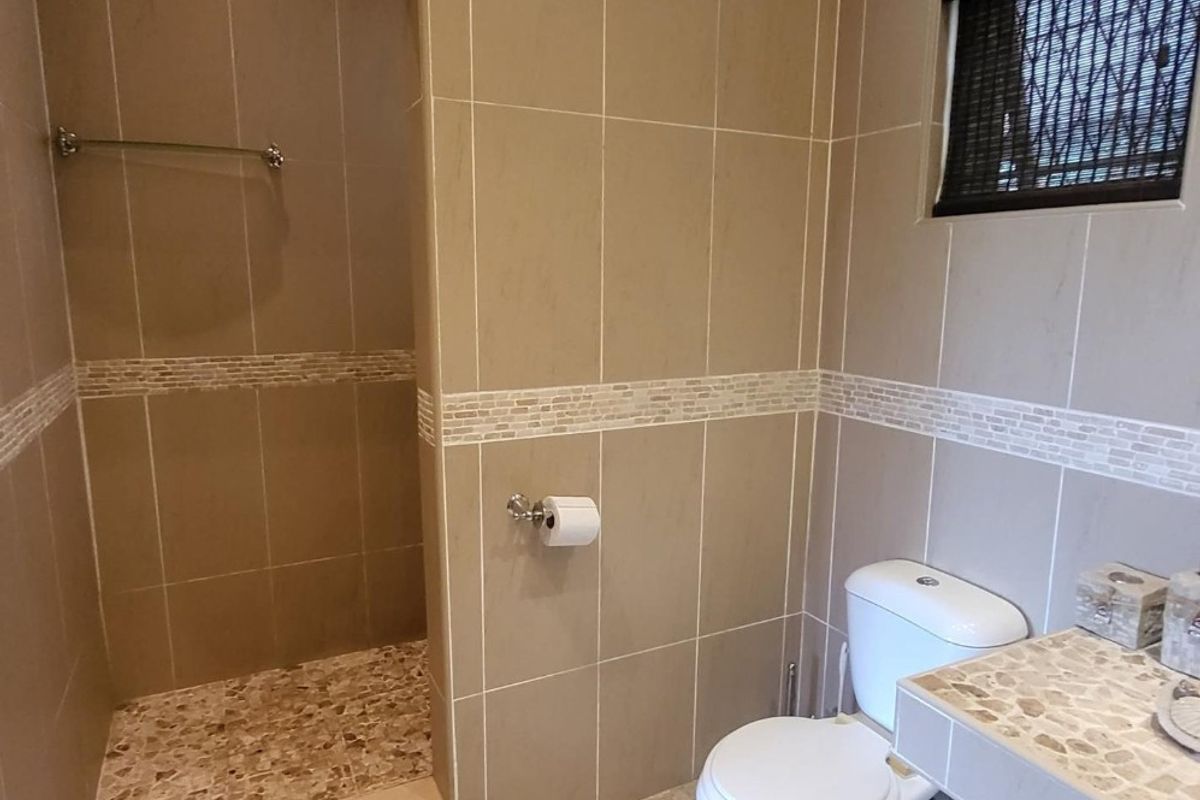 A clean, neutral-toned bathroom featuring a walk-in shower, tiled walls with mosaic accents, and a built-in vanity unit.