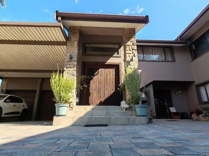 Front elevation of the house featuring a stone-clad entrance, timber door, and a paved driveway with an attached carport.