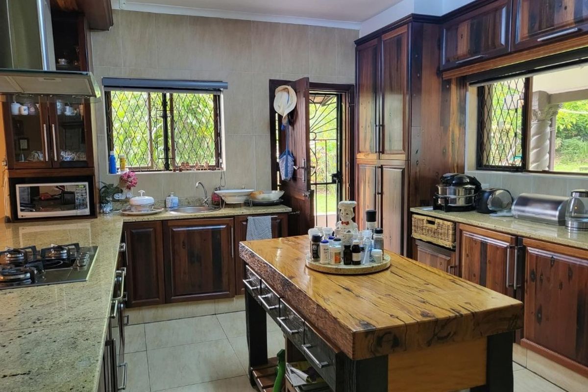 A traditional kitchen featuring dark wood cabinetry, granite countertops, a central wooden island, and a built-in gas hob with an extractor fan.
