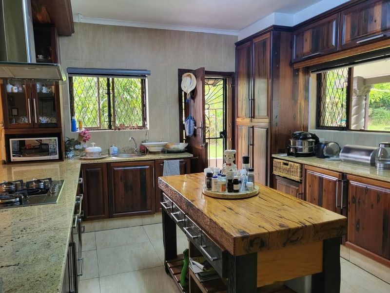 A traditional kitchen featuring dark wood cabinetry, granite countertops, a central wooden island, and a built-in gas hob with an extractor fan.