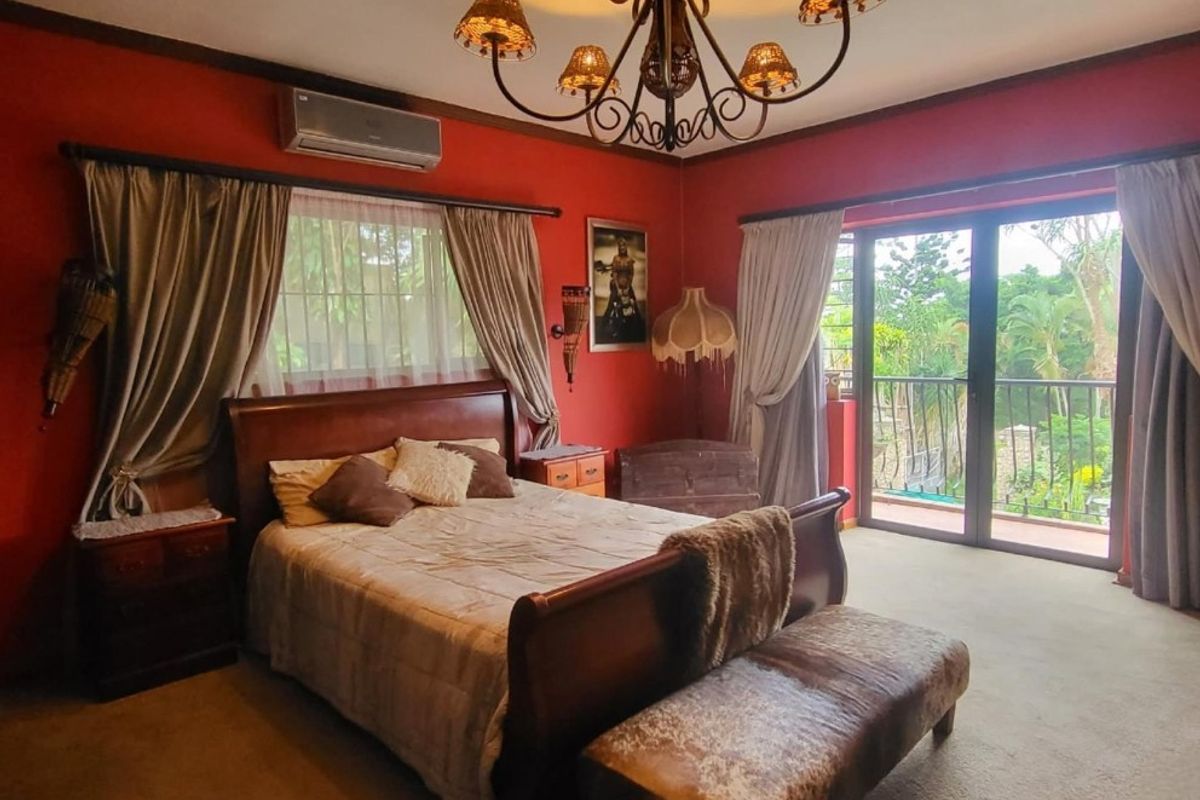 Spacious bedroom featuring red walls, carpeted flooring, a decorative chandelier, and sliding glass doors providing access to a private balcony.