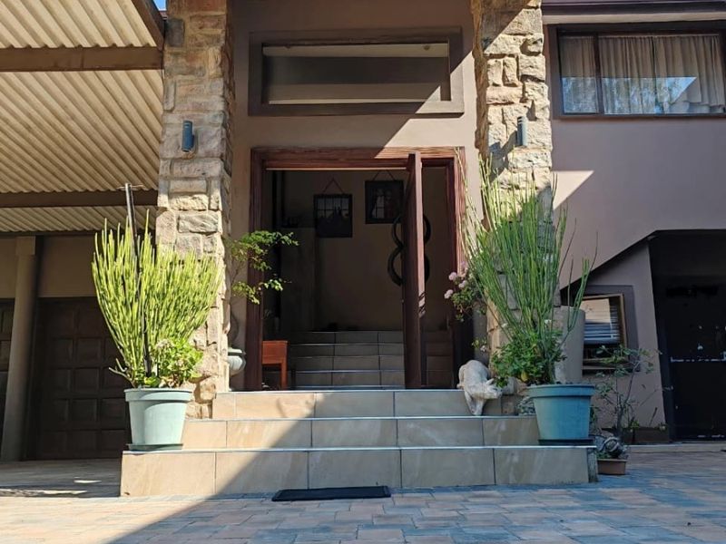 Front entrance of the house featuring stone cladding, tiled steps, and a paved driveway with an adjacent covered carport area.