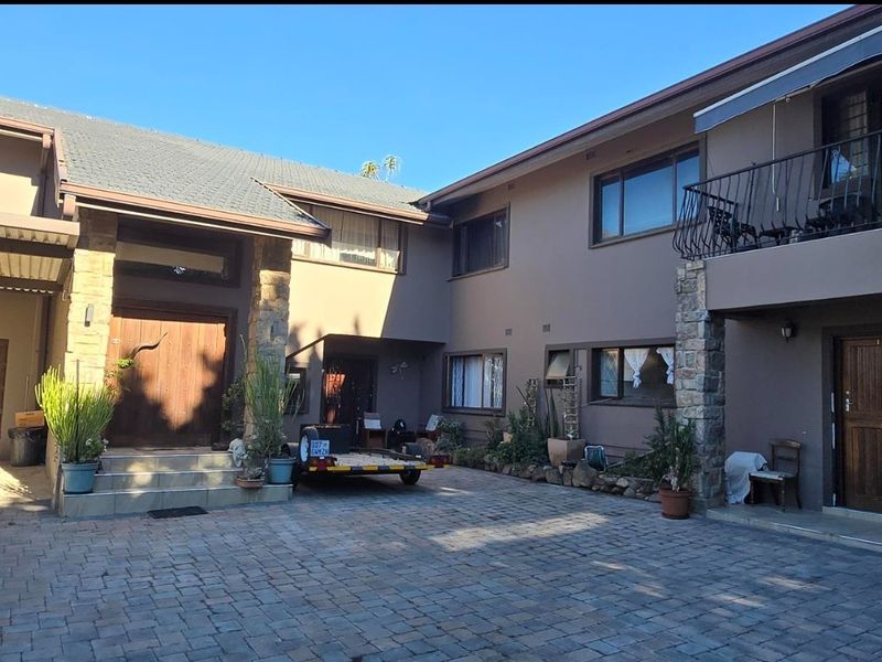 Front exterior view of a double-storey house featuring a paved driveway, stone-clad pillars, and a balcony with metal railings.