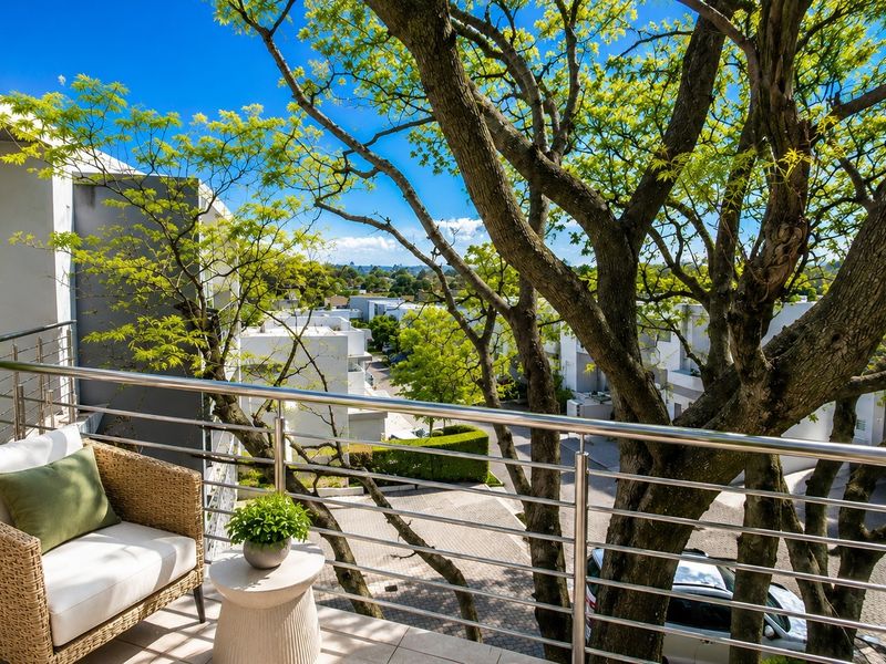 A modern balcony featuring a sleek stainless steel balustrade and tiled flooring, offering a pleasant elevated view of the surrounding neighbourhood and mature trees.