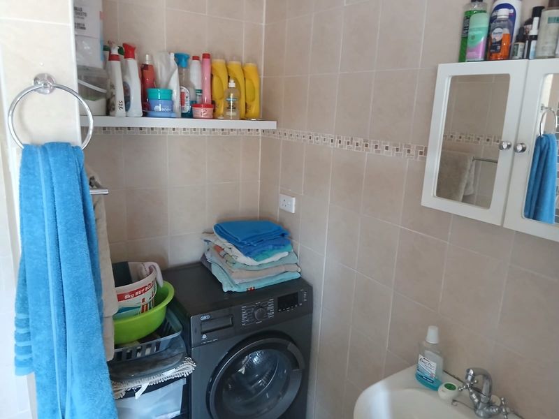 A functional laundry area featuring ceramic wall tiles, a built-in wash basin with chrome fixtures, and wall-mounted storage shelving.