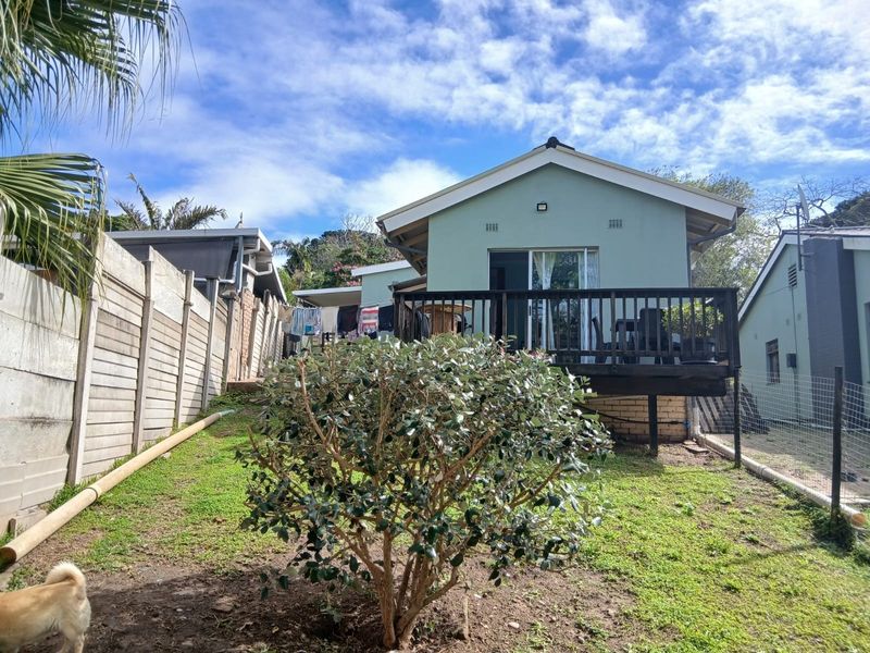 Rear view of the cottage featuring a raised timber deck, sliding glass doors, and a private garden area with boundary walling.